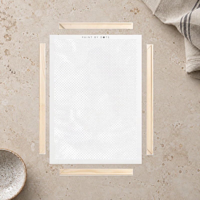 Kit cadre en bois pour toile, présenté sur un plan de travail en pierre claire près d’un tissu en lin.